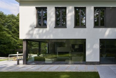 Renovace rodinného domu v německém městě Bergisch Gladbach - Přechod mezi zahradou a domem tvoří betonové desky a rýnský štěrkopísek. Tmavé rámové profily prosklených ploch kontrastují se světlými povrchy.