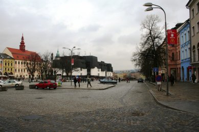 Věda, architekti a památky - <B>Regenerace a dialog počesku</B>: Zdeněk Sklepek, obchodní dům Prior, Jihlava, 1978-83, foto 2008. Nositel titulu CSc. rozčlenil hmoty pomocí „domovních“ oken a falešných střech tak dětinsky, až se pozorovateli téměř nechce věřit, že za tím nestojí nějaký obzvlášť rafinovaný koncept. Možná první příklad tzv. podnikatelského baroka u nás. Stromy zbytečně zakrývají historické fasády, zatímco obchodní dům a zásobovací rampy rozrývající povrch náměstí zůstávají odkryté. - foto: Martin Horáček