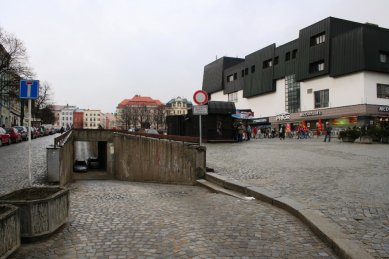 Věda, architekti a památky - <B>Regenerace a dialog počesku</B>: Zdeněk Sklepek, obchodní dům Prior, Jihlava, 1978-83, foto 2008. Nositel titulu CSc. rozčlenil hmoty pomocí „domovních“ oken a falešných střech tak dětinsky, až se pozorovateli téměř nechce věřit, že za tím nestojí nějaký obzvlášť rafinovaný koncept. Možná první příklad tzv. podnikatelského baroka u nás. Stromy zbytečně zakrývají historické fasády, zatímco obchodní dům a zásobovací rampy rozrývající povrch náměstí zůstávají odkryté. - foto: Martin Horáček
