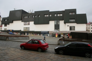 Věda, architekti a památky - <B>Regenerace a dialog počesku</B>: Zdeněk Sklepek, obchodní dům Prior, Jihlava, 1978-83, foto 2008. Nositel titulu CSc. rozčlenil hmoty pomocí „domovních“ oken a falešných střech tak dětinsky, až se pozorovateli téměř nechce věřit, že za tím nestojí nějaký obzvlášť rafinovaný koncept. Možná první příklad tzv. podnikatelského baroka u nás. Stromy zbytečně zakrývají historické fasády, zatímco obchodní dům a zásobovací rampy rozrývající povrch náměstí zůstávají odkryté. - foto: Martin Horáček