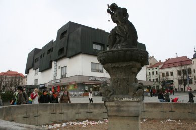 Věda, architekti a památky - <B>Regenerace a dialog počesku</B>: Zdeněk Sklepek, obchodní dům Prior, Jihlava, 1978-83, foto 2008. Nositel titulu CSc. rozčlenil hmoty pomocí „domovních“ oken a falešných střech tak dětinsky, až se pozorovateli téměř nechce věřit, že za tím nestojí nějaký obzvlášť rafinovaný koncept. Možná první příklad tzv. podnikatelského baroka u nás. Stromy zbytečně zakrývají historické fasády, zatímco obchodní dům a zásobovací rampy rozrývající povrch náměstí zůstávají odkryté. - foto: Martin Horáček